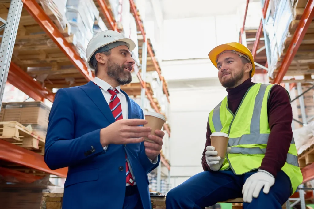 In einem Lagerhaus unterhalten sich zwei Kollegen in Hi-Vis Kleidung